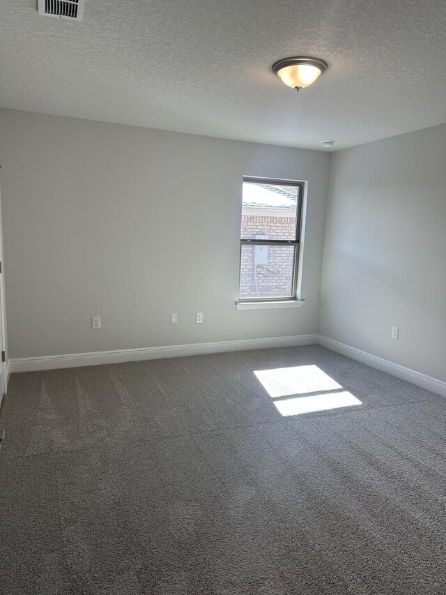 empty room with a textured ceiling, dark carpet, visible vents, and baseboards