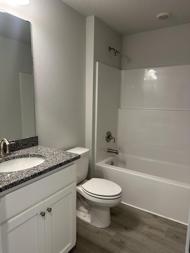 bathroom featuring a textured ceiling, toilet, wood finished floors, vanity, and shower / bathing tub combination