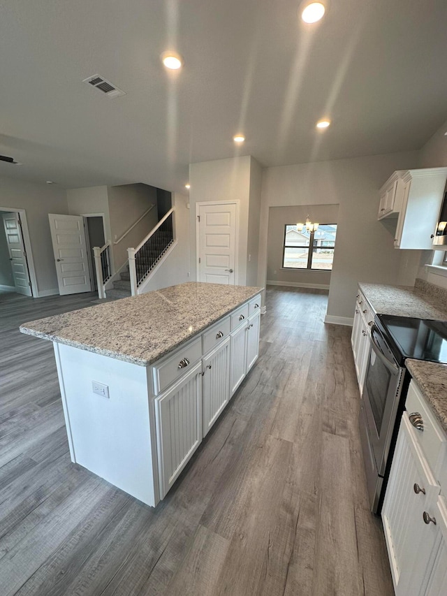 kitchen with hardwood / wood-style floors, a kitchen island, light stone counters, white cabinets, and stainless steel range with electric cooktop