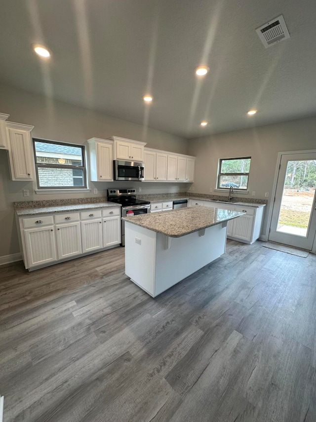 kitchen featuring hardwood / wood-style floors, a kitchen bar, appliances with stainless steel finishes, a kitchen island, and white cabinetry