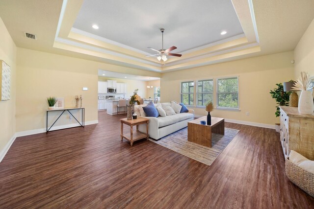 living room with dark hardwood / wood-style flooring, a raised ceiling, crown molding, and ceiling fan