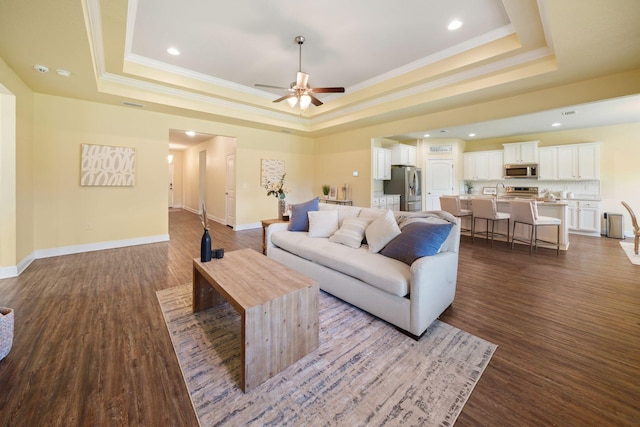 living room featuring a tray ceiling, ceiling fan, crown molding, and wood-type flooring