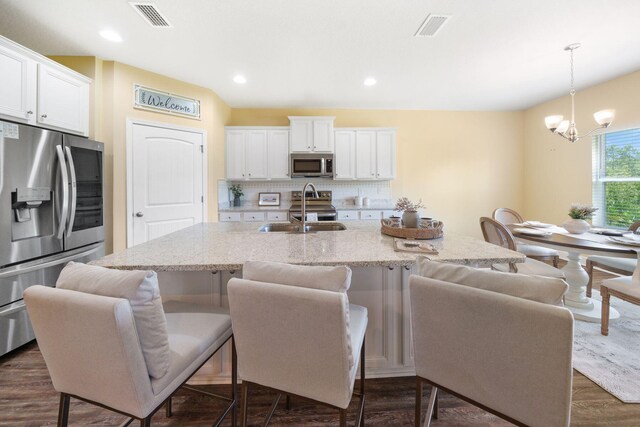 kitchen with appliances with stainless steel finishes, decorative backsplash, dark hardwood / wood-style floors, light stone countertops, and a notable chandelier