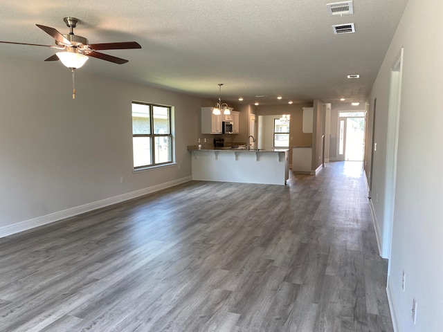 unfurnished living room featuring ceiling fan with notable chandelier, a wealth of natural light, hardwood / wood-style flooring, and sink