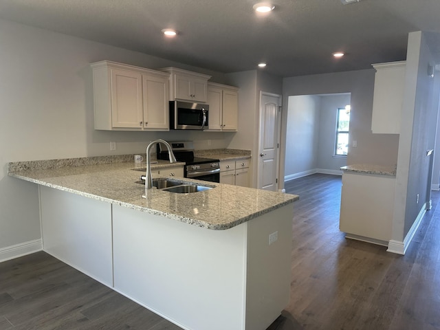 kitchen featuring appliances with stainless steel finishes, dark wood-type flooring, a peninsula, white cabinetry, and a sink