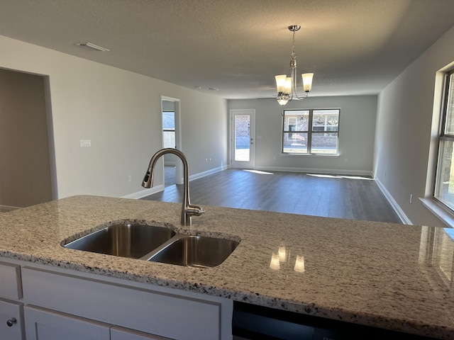 kitchen featuring a sink, visible vents, open floor plan, light stone countertops, and pendant lighting