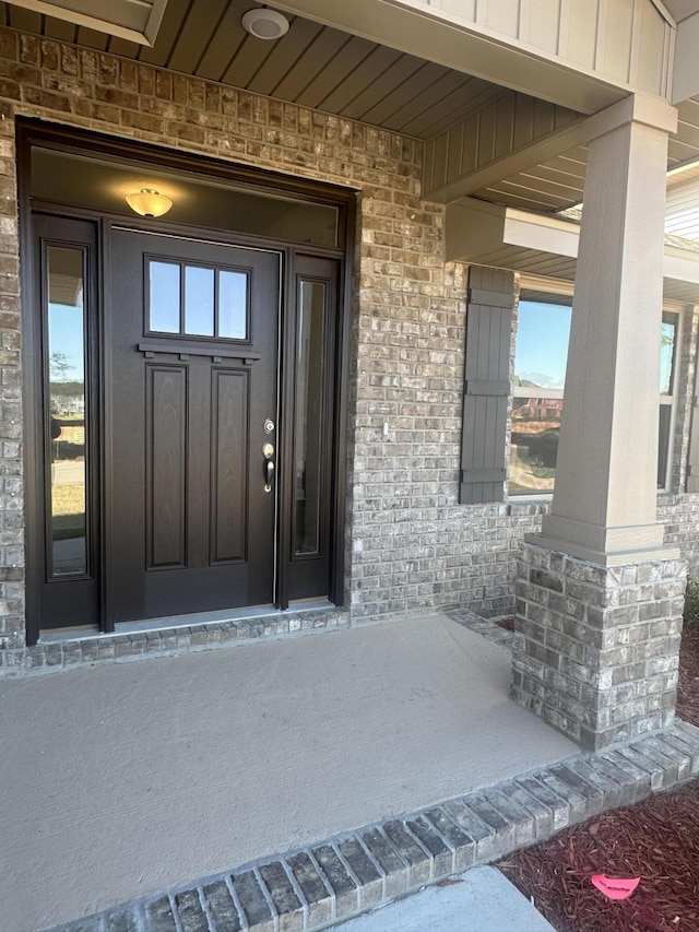 doorway to property featuring a porch and brick siding