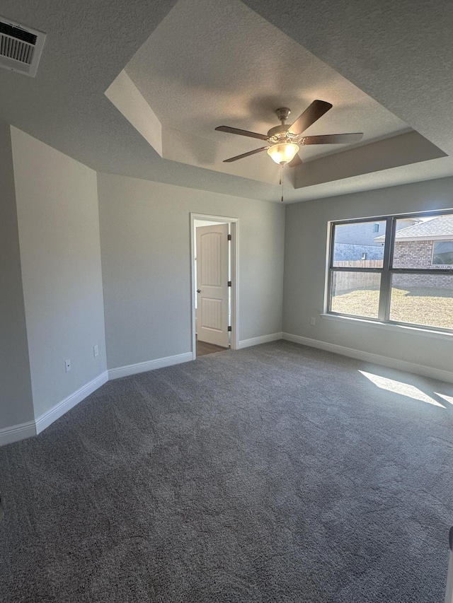 empty room with a textured ceiling, a tray ceiling, visible vents, and baseboards