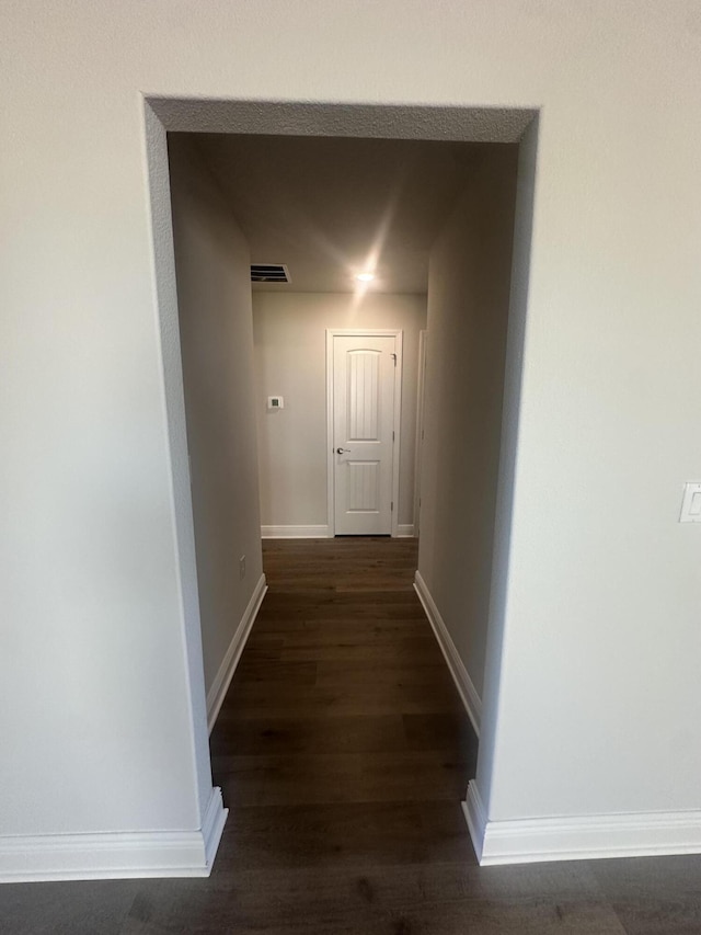 hall with visible vents, baseboards, and dark wood-style flooring