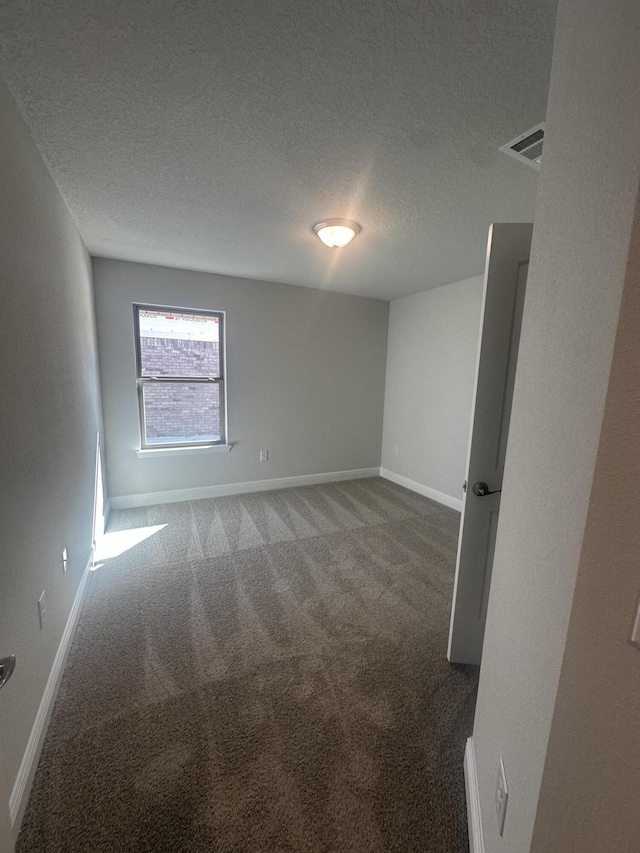 empty room with visible vents, dark carpet, a textured ceiling, and baseboards