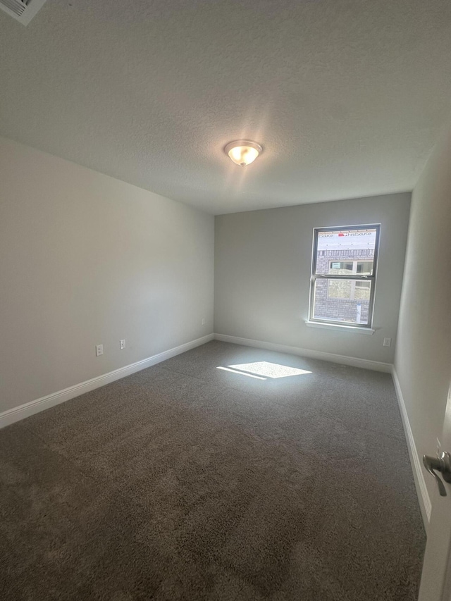 empty room featuring dark colored carpet, a textured ceiling, and baseboards