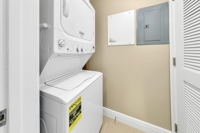 laundry room featuring light tile patterned floors, stacked washer / dryer, laundry area, electric panel, and baseboards