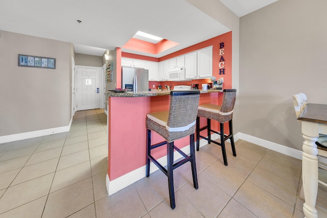 kitchen with a breakfast bar, light tile patterned floors, white microwave, white cabinetry, and stainless steel fridge with ice dispenser