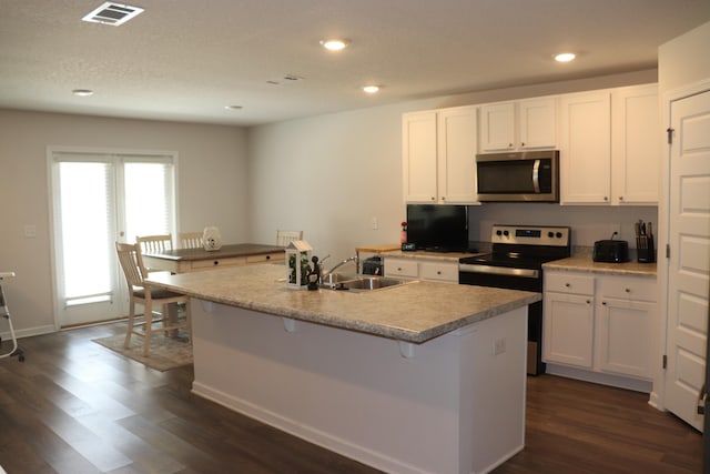 kitchen featuring sink, dark wood-type flooring, white cabinetry, stainless steel appliances, and a center island with sink