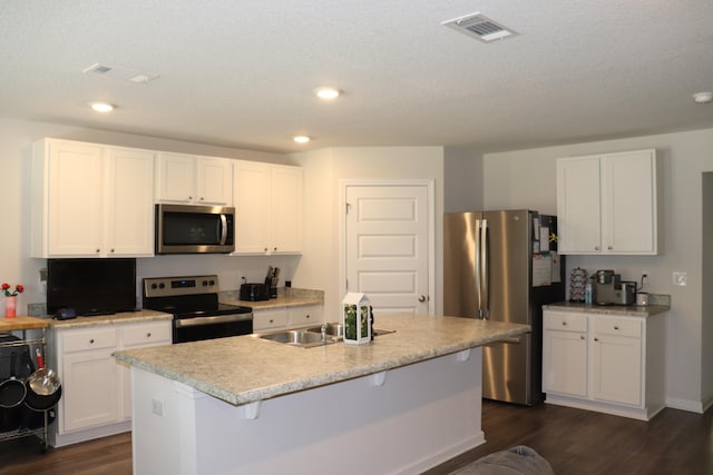 kitchen featuring stainless steel appliances, white cabinetry, a kitchen island with sink, dark hardwood / wood-style flooring, and a breakfast bar area