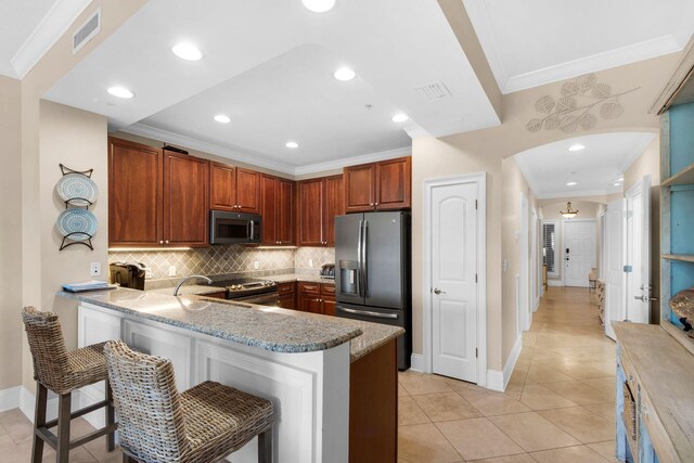 kitchen with appliances with stainless steel finishes, light tile patterned flooring, kitchen peninsula, and a kitchen breakfast bar