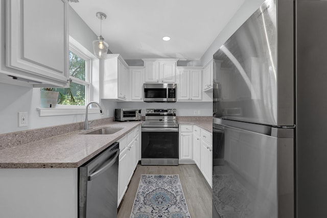 kitchen with light wood-type flooring, pendant lighting, white cabinetry, stainless steel appliances, and sink