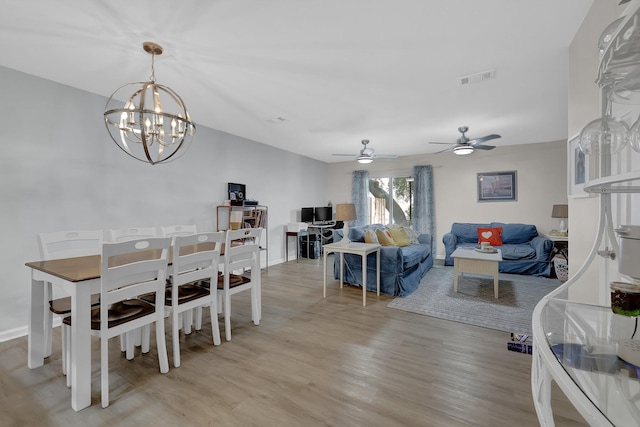 dining space with ceiling fan with notable chandelier and light hardwood / wood-style floors