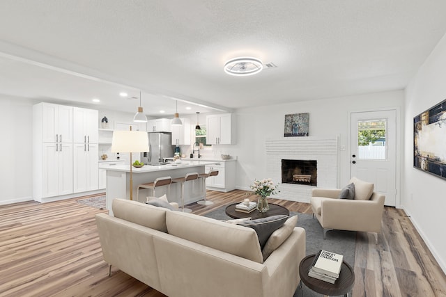 living room with light hardwood / wood-style floors, a textured ceiling, a fireplace, and sink