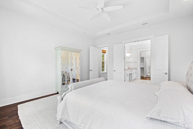 bedroom with ceiling fan, dark hardwood / wood-style floors, ensuite bath, and a raised ceiling