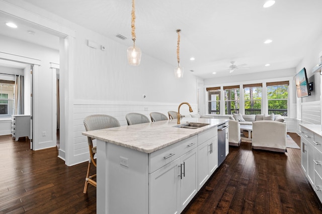 kitchen with stainless steel dishwasher, sink, a center island with sink, dark hardwood / wood-style flooring, and a kitchen breakfast bar