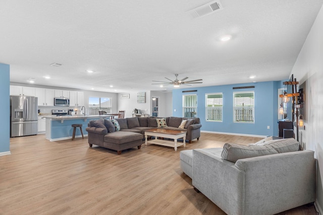 living room featuring ceiling fan, sink, and light hardwood / wood-style floors