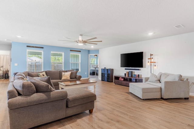 living room with ceiling fan, light wood-type flooring, and a textured ceiling