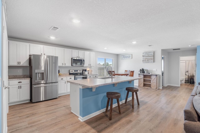 kitchen featuring sink, appliances with stainless steel finishes, light hardwood / wood-style flooring, an island with sink, and white cabinets