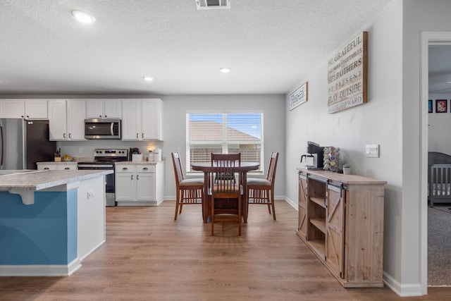 kitchen featuring stainless steel appliances, light hardwood / wood-style floors, white cabinets, and a breakfast bar