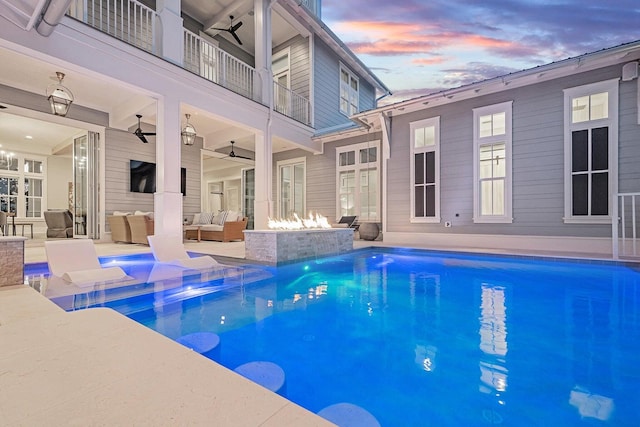 pool at dusk with ceiling fan, an outdoor living space, and a patio