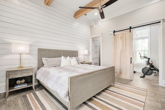 bedroom with beamed ceiling, wood walls, a barn door, light hardwood / wood-style flooring, and ceiling fan