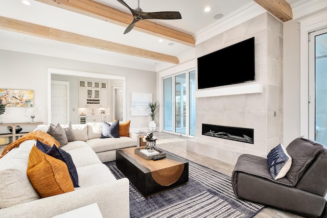 living room with ceiling fan, beamed ceiling, crown molding, and a tile fireplace