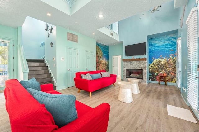 living room featuring light wood-type flooring, a stone fireplace, a high ceiling, and a textured ceiling