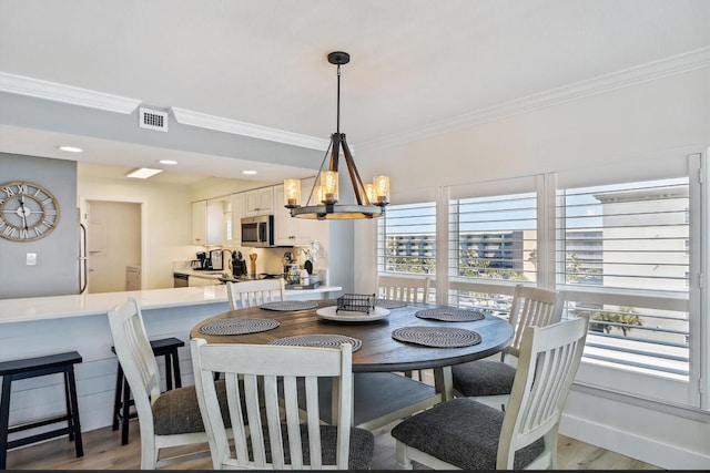 dining room with light wood-type flooring, a notable chandelier, and ornamental molding