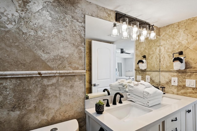 bathroom with ceiling fan, toilet, vanity, and tile walls