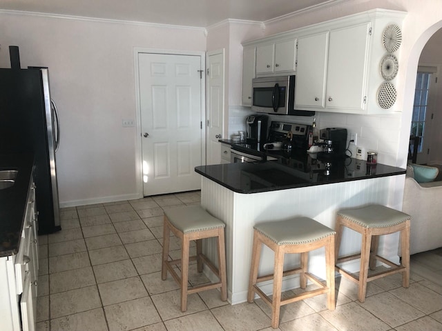 kitchen featuring tasteful backsplash, a kitchen bar, kitchen peninsula, appliances with stainless steel finishes, and white cabinets