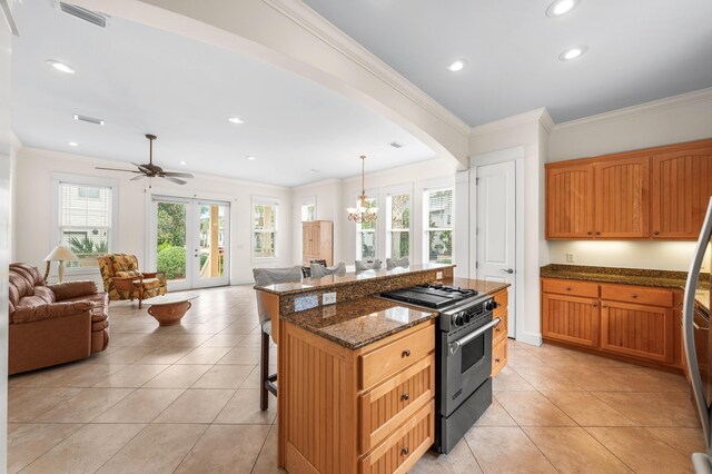 kitchen with a breakfast bar area, ceiling fan with notable chandelier, a center island, high end stove, and dark stone counters