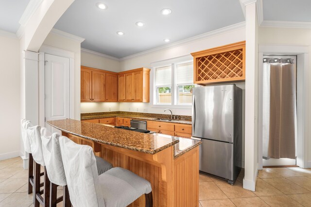 kitchen with dark stone countertops, stainless steel refrigerator, crown molding, a kitchen island, and a breakfast bar