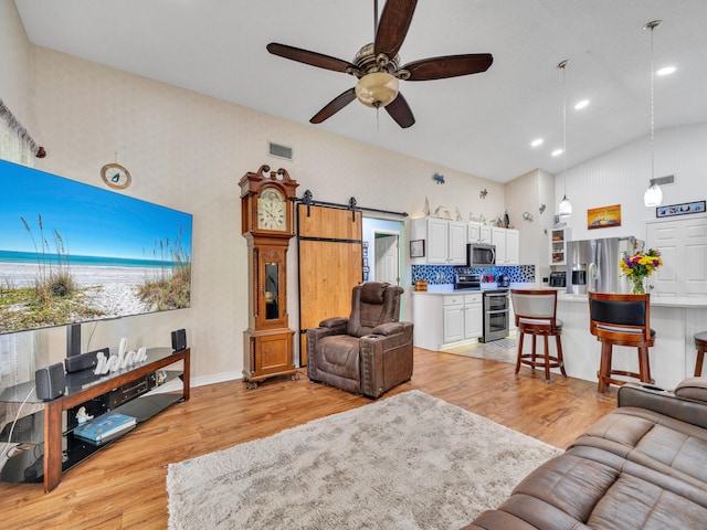 living room featuring light wood-type flooring, a barn door, high vaulted ceiling, and ceiling fan