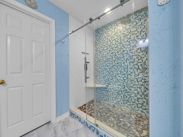 bathroom featuring marble finish floor, a textured wall, a textured ceiling, and a stall shower