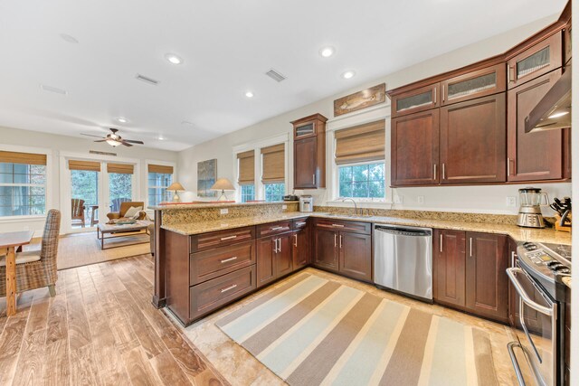 kitchen featuring light wood-type flooring, light stone counters, ceiling fan, stainless steel appliances, and kitchen peninsula