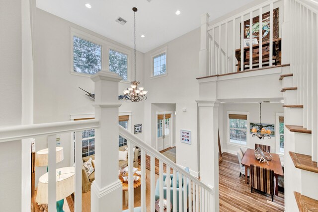 hall featuring a wealth of natural light, hardwood / wood-style floors, an inviting chandelier, and a towering ceiling