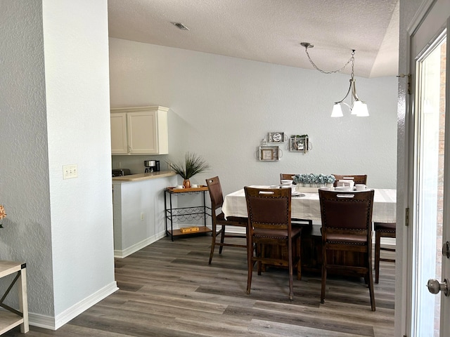 dining area with a textured ceiling, dark wood-type flooring, and a chandelier