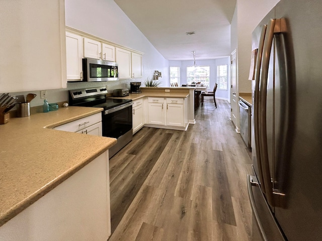 kitchen featuring dark wood-type flooring, decorative light fixtures, kitchen peninsula, lofted ceiling, and stainless steel appliances