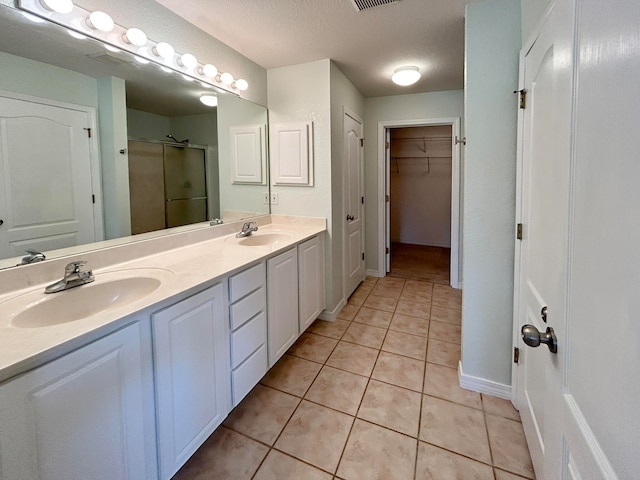 bathroom with a textured ceiling, a shower with door, vanity, and tile patterned floors