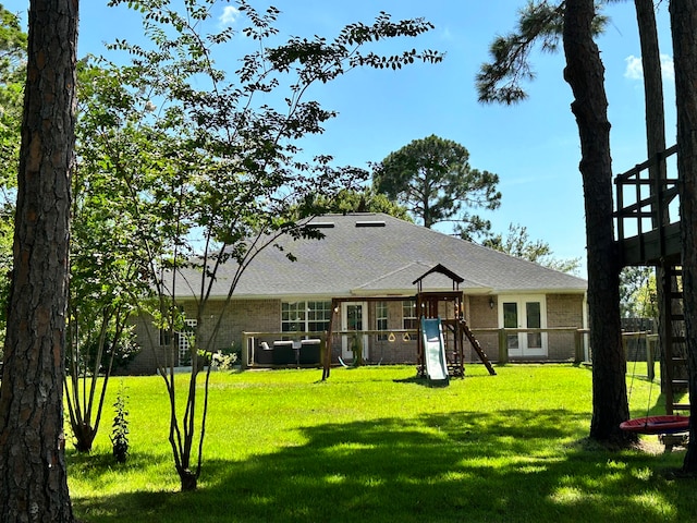 rear view of property with a playground and a yard