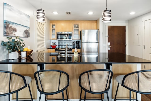 kitchen featuring light brown cabinets, decorative backsplash, hanging light fixtures, and stainless steel appliances