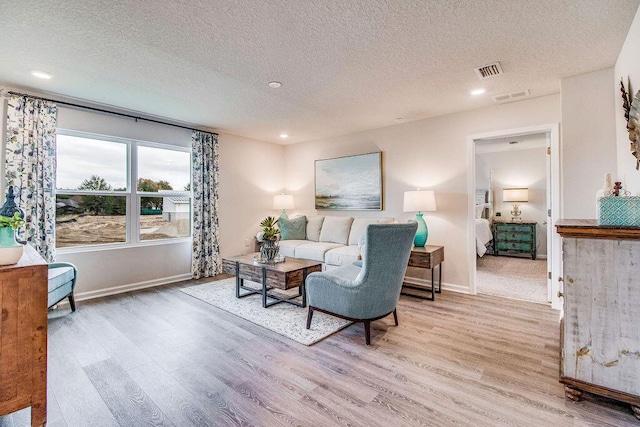 living room with a textured ceiling, light wood-type flooring, and visible vents