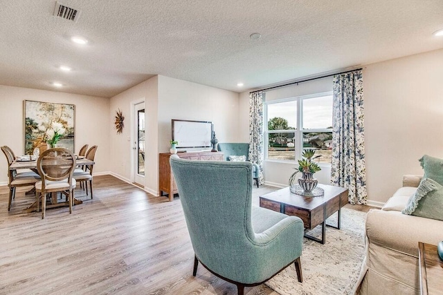 living room with a textured ceiling, recessed lighting, visible vents, baseboards, and light wood-style floors