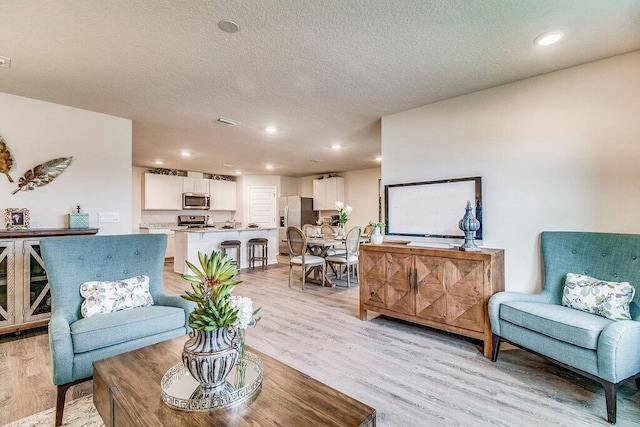 living area with light wood-style floors, visible vents, a textured ceiling, and recessed lighting